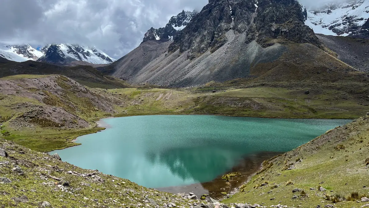 A turquoise lagoon beneath rock spires and glaciers on the Ausangate trek