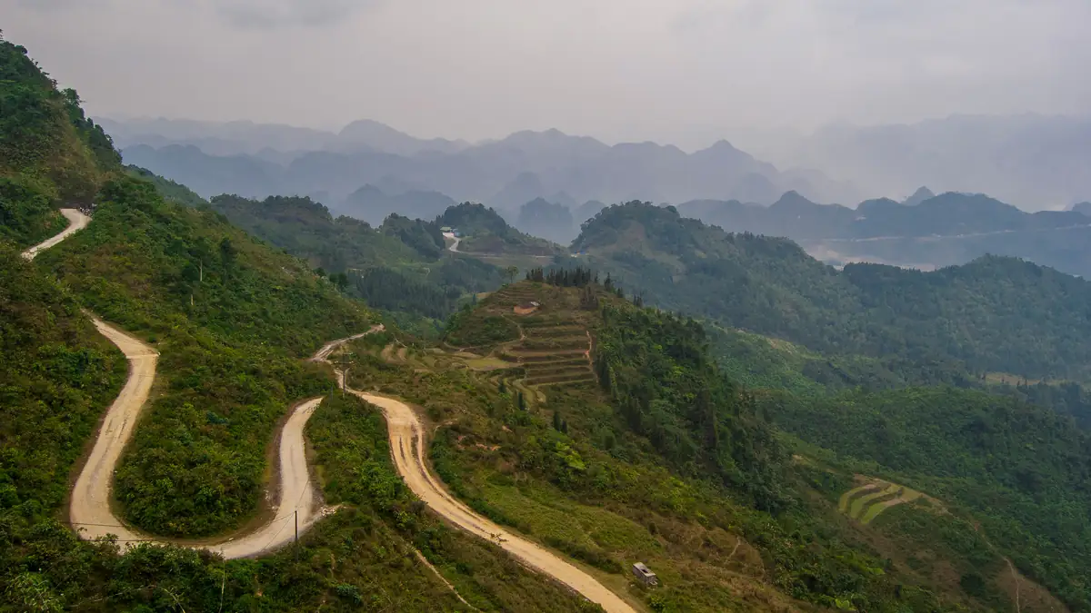 Hairpin bends of a gravel road through the green mountains of Ha Giang