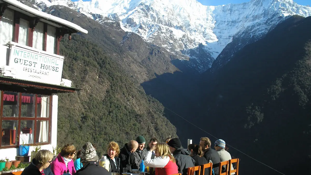 Gäste beim Essen auf der Terrasse einer Lodge in Chhomrong mit Bergblick