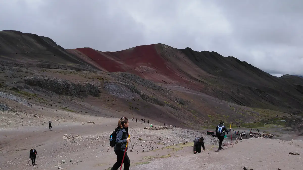 Hikers on the wide trail to Vinicunca, the red ridge behind